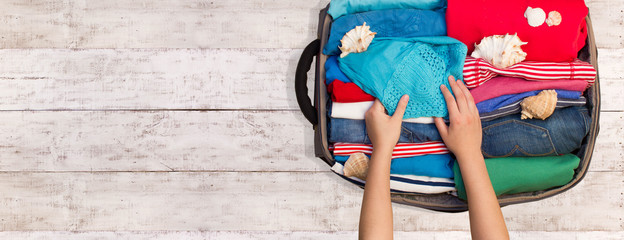 Woman packing luggage for a new journey on a wooden floor. Place for your text.