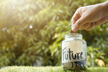 Money saving, Hand putting coin in glass jar with coins inside For now and future money. Concept of saving money for future. - 155336879