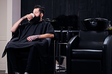 A man drinks coffee in a hairdresser's salon.
