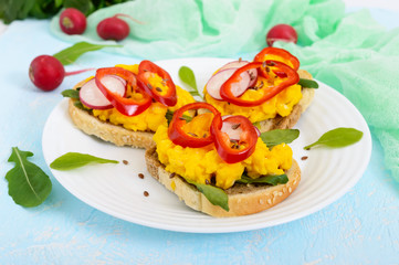 Sandwich with scrambled eggs, rucola, radish, paprika kapi and flax seeds on a plate on a light background. Fast and tasty breakfast.