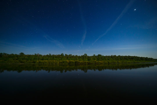 The stars in the night sky are reflected in the river. . The landscape is photographed by moonlight.