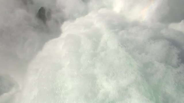 AERIAL TOP DOWN CLOSE UP: Flying above the raging whitewater river dropping over the steep cliff of Niagara Falls crashing on the rocky bottom. Rainbow arc over violent, misty, foamy Horseshoe Falls 