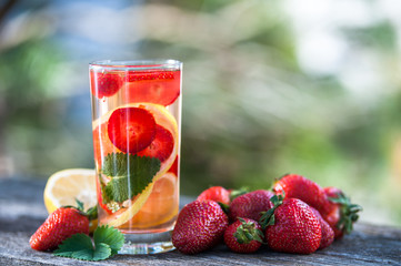 A glass of  detox water. Strawberry, lemon and mint with cool clean water, backdrop of a green garden. Detox, diet, Cookery, sports, proper nutrition, sports nutrition, body cleansing
