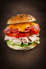 Delicious sandwich with ham, lettuce, tomato, chicken and cheddar cheese on a wooden table