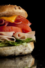Delicious sandwich with ham, lettuce, tomato, chicken and cheddar cheese on a wooden table