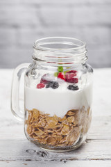 Cereals, yogurt and red fruits in a mason jar on a white wooden table