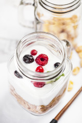 Cereals, yogurt and red fruits in a mason jar on a white wooden table