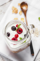 Cereals, yogurt and red fruits in a mason jar on a white wooden table