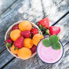 Basket strawberries and apricots, top view, glass with strawberry smoothies and strawberry leaves, natural wood background. Detox, diet, Cookery, Proper nutrition, sports nutrition, body cleansing.
