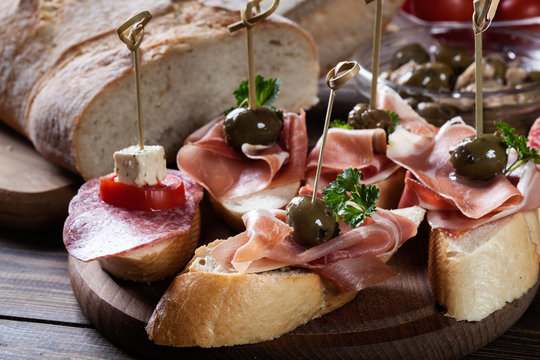 Spanish tapas with slices jamon serrano, salami, olives and cheese cubes on a wooden table