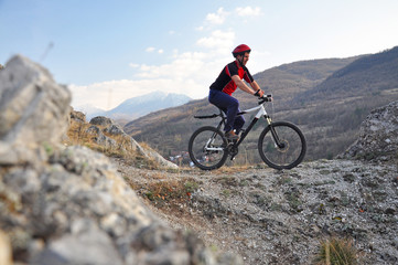 Fototapeta na wymiar Young man riding a bike on hill under a mountain, extreme riding bicycle off road on rocks