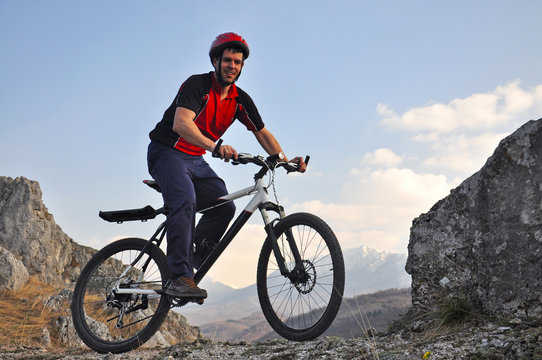 Young man riding a bike on hill under a mountain, extreme riding bicycle off road on rocks