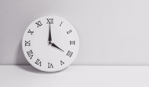 Closeup white clock for decorate in 4 o'clock on white wood desk and wallpaper textured background in black and white tone with copy space