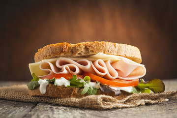 Tasty sandwich with ham, cheese, tomato and lettuce on wooden background