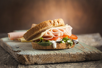 Leckeres Sandwich mit Schinken, Käse, Tomaten und Salat auf Holzuntergrund