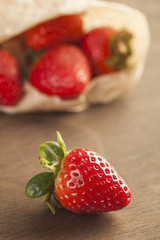 Strawberries in a paper bag on dark wooden background