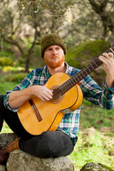 Hipster man with red beard playing a guitar