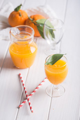 Orange juice in glass and jar over white wooden table
