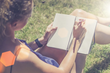 Summer sunny day. Close-up of a notebook in the hands of a young woman sitting in the park on the lawn.