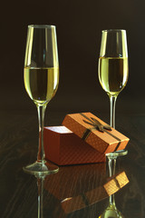 Two glass with champagne or white wine and gift box on mirror table. Celebrities composition. Selective focus