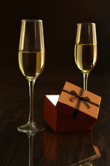 Two glass with champagne or white wine and gift box on mirror table. Celebrities composition. Selective focus