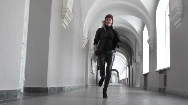 Woman hooligan runs along a long corridor, she runs away.