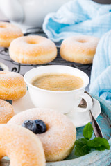 Cup of coffee and homemade donuts with powdered sugar and fresh blueberries on light gray background. Selective focus.