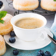 Cup of coffee and homemade donuts with powdered sugar and fresh blueberries on light gray background. Selective focus.