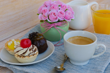 Cup of tea with milk, cute sweet cake, orange juice on wooden background. Good morning surprise concept. 