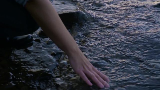 Closeup Of Woman's Hand Playing In Water On Rocky Shoreline At Sunset