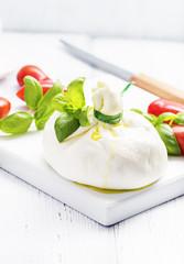 Italian burrata cheese with basil onion olive oil on white   plate on light background. Selective focus, free text space.