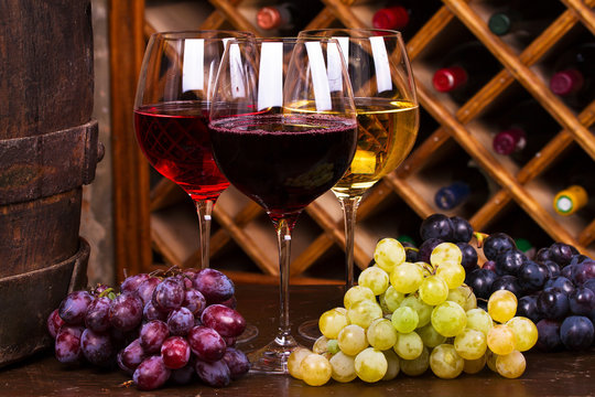 Glasses of red, rose and white wine with cheese, and grape in wine cellar.  Food and drinks concept