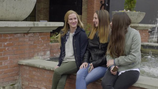 Group Of Friends Sit On Edge Of Fountain And Chat And Laugh Together