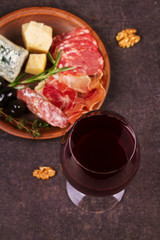 Glass of red wine with cheese, prosciutto and salami. Wine and cheese still life. Food and drinks concept. View from above, top studio shot