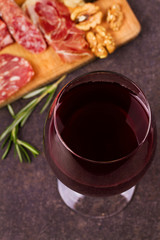 Glass of red wine with cheese, prosciutto and salami. Wine and cheese still life. Food and drinks concept. View from above, top studio shot