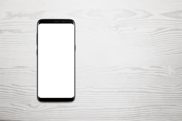 Black mobile phone on white wooden desk with free space for text. Isolated white screen for mockup.