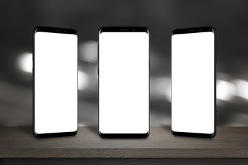 Three mobile phones with isolated screen for mockup on the table. Bokeh lights in background.