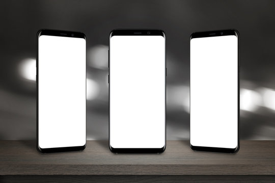 Three Mobile Phones With Isolated Screen For Mockup On The Table. Bokeh Lights In Background.