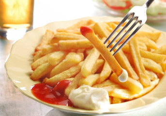 French fries ketchup mayo with salad and glass of beer. Selective focus on fork.