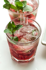 Tasty cold fresh drink lemonade with raspberry, mint, ice and lime in glass on white plate with ice background. Closeup.