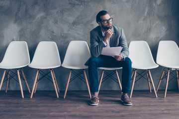 Close up of concentrated pensive bearded guy in formal wear and glasses. He is sitting in the hall...