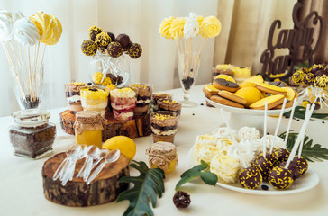 Holiday candy bar in yellow and brown color. Wedding candy bar served with cupcakes, cake pops, desserts in glasses, lemons and coffee beans