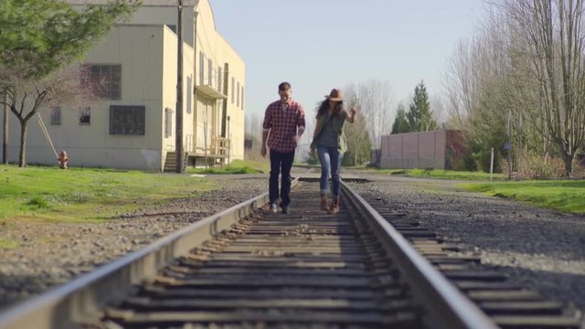 Carefree Couple Walk Playfully Down Train Tracks Toward Camera