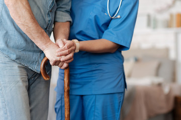 Kind trained nurse helping feeble gentleman walking