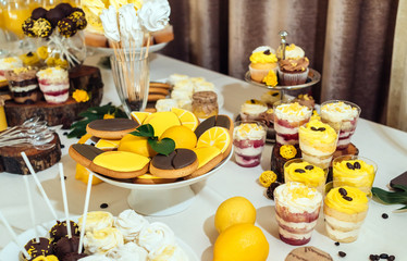 Holiday candy bar in yellow and brown color. Wedding candy bar served with lemon biscuits, cake pops, desserts in glasses, lemons and coffee beans