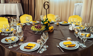 Wedding flower arrangement of yellow roses, greenery and lemons on stump under table number card on wedding dinner table. Number of guest table at wedding banquet