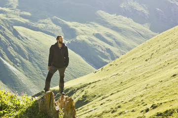 man in black jacket standing on stone with hands-up above mountais at sunset