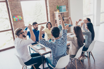 Success and team work concept. Team of business partners with raised up hands in light modern workstation, celebrating the breakthrough in their company