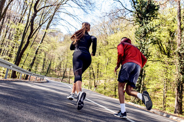 Back view of young athletic couple running in woods.