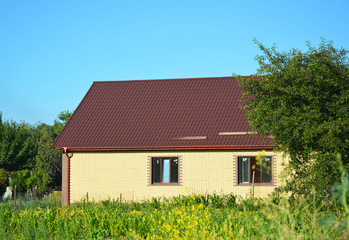 Cozy brick house with metal roof in green garden. Metal Roof repair, Roofing construction
